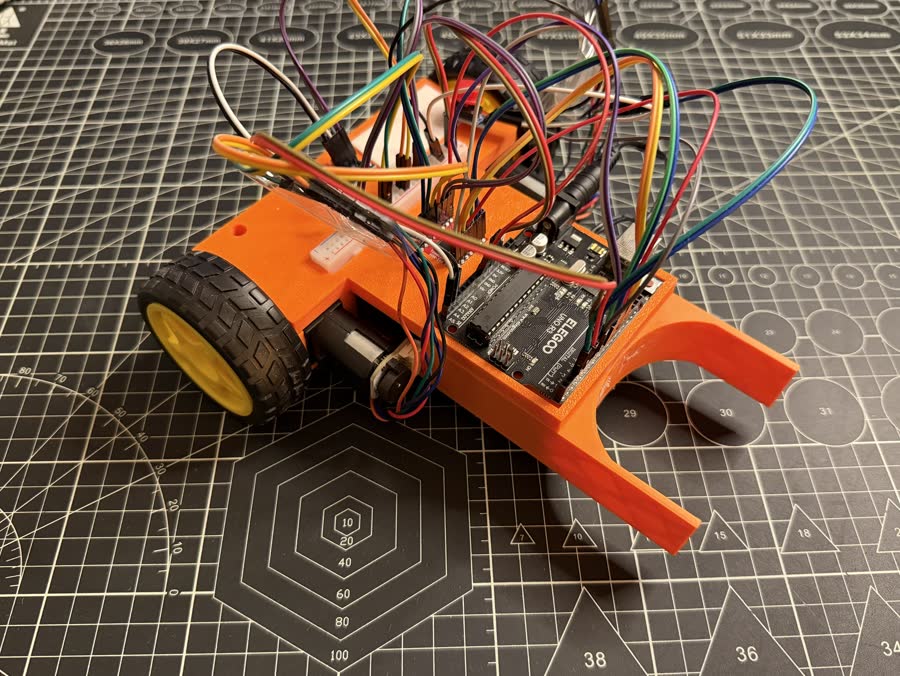 Orange 3D-printed robot car with an extended front guide arm and an Elegoo Arduino Uno.